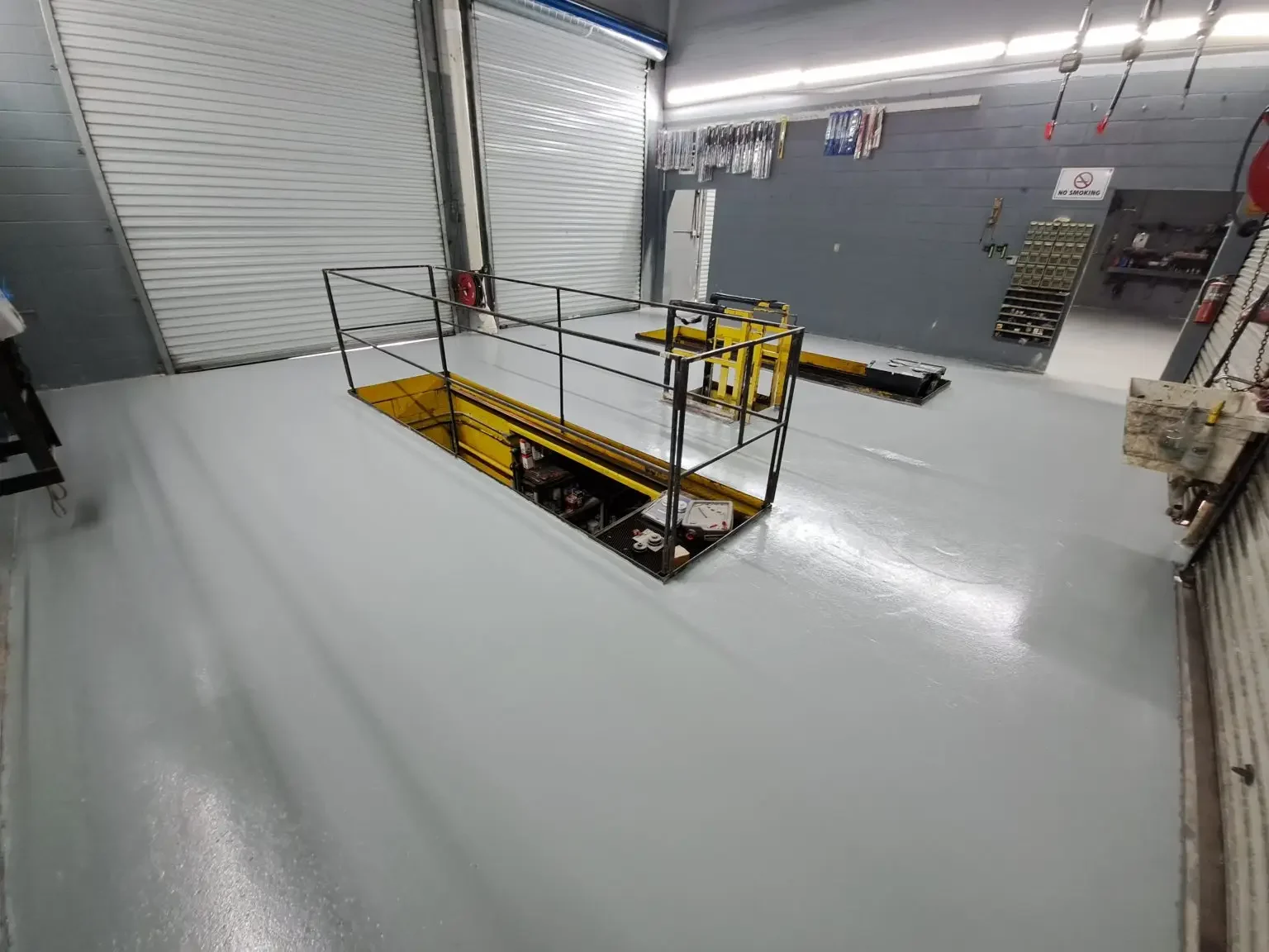 Gray solid color epoxy floor in an auto shop around an in-ground vehicle lift