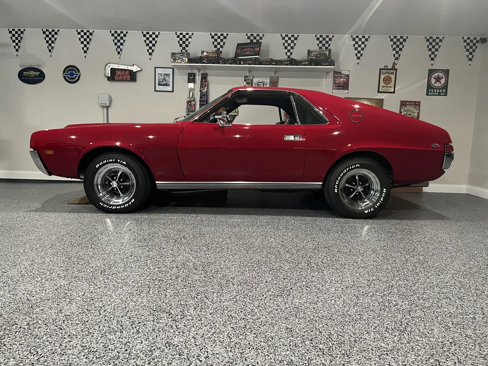Gray flake epoxy garage floor under a red classic car, checkered pennants on the wall