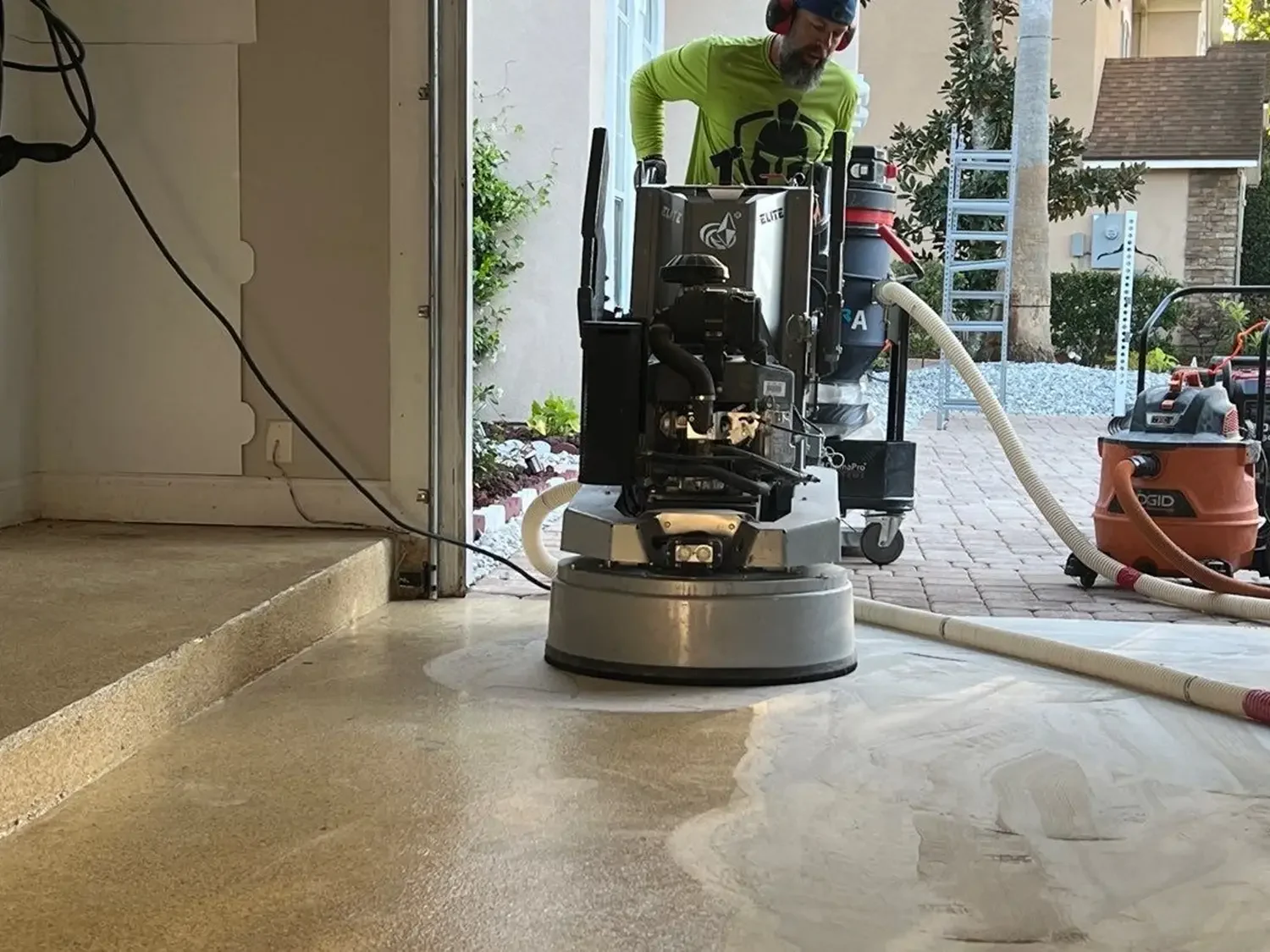 Spartan crew member running a diamond grinder with a dust vacuum on a garage slab